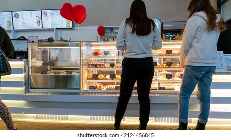 Grodno, Belarus, January 2, 2022: Shoppers Walk Near A Display Case With Sweets In A Cafe. Visitors Choose A Delicious Cake And Coffee In The City Cafe. Time Lapse People In A Shop