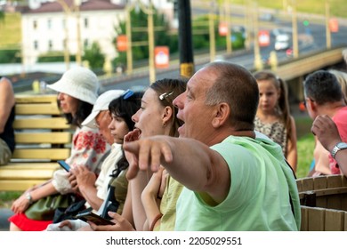 Grodno, Belarus July 10, 2022: An Elderly Man With His Family Is Resting In The Park Sitting On A Bench. A Pensioner With His Granddaughter At An Outdoor Concert. The Man Smiles Cheerfully