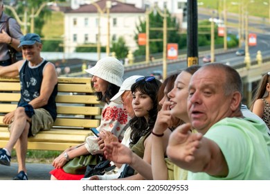 Grodno, Belarus July 10, 2022: An Elderly Man With His Family Is Resting In The Park Sitting On A Bench. A Pensioner With His Granddaughter At An Outdoor Concert. The Man Smiles Cheerfully