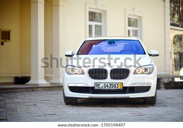 Grodno, Belarus, May 2013: Modern luxury BMW\
750Li XDrive car front view parked on stone paved parking near\
ancient house\
horizontal.