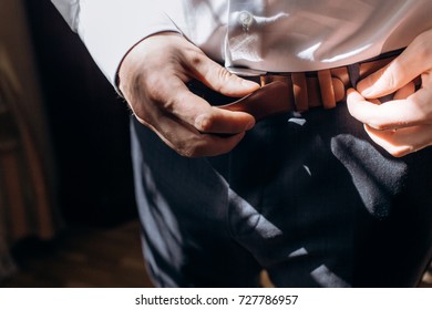 Groom adjusting stylish brown leather belt during morning before wedding, handsome man in elegant suit putting on belt before meeting closeup - Powered by Shutterstock