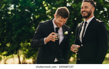 Groom and best man drinking and smiling during wedding party. Groom and groomsmen partying after wedding.