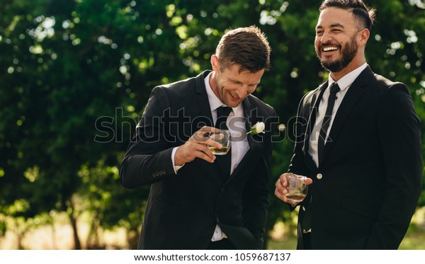 Groom and best man\
drinking and smiling during wedding party. Groom and groomsmen\
partying after wedding.
