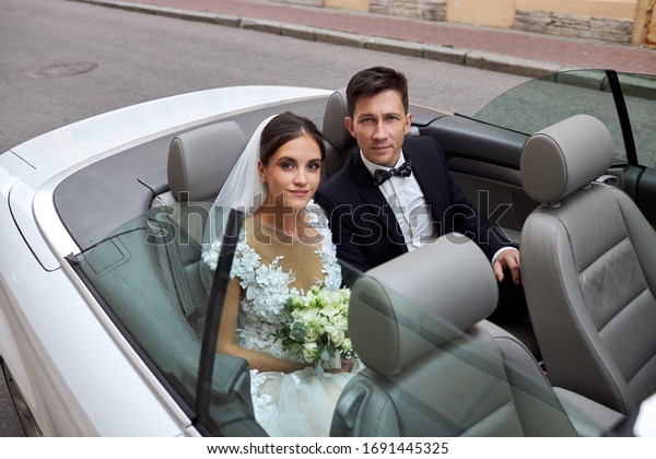 the groom in a black suit and the\
bride in a white dress are sitting in the back seat of a\
car