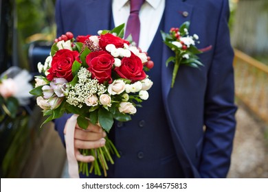 The groom in a blue suit holds a beautiful bridal bouquet in his right hand. Selective focus. Blur the background.