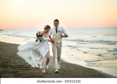 Groom and bride run along the shore against the wind