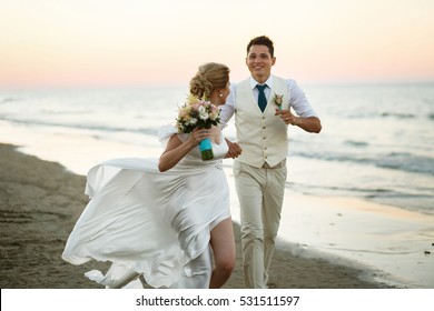 Groom and bride run along the shore against the wind