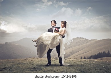 Groom carrying his wife in his arms on a hill