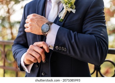 Groom fixing his cufflinks. Handsome groom dressed in dark blue formal suit getting ready for wedding. Elegant groom wedding fashion.