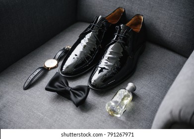The groom is gathering in the morning. A gray chair.  Men's Black classic patent leather shoes. A black bow tie. Wedding details. Eau de toilette, perfume, watch with leather strap. - Powered by Shutterstock