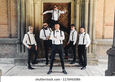 Groom and groomsmen in black trousers pose between columns - Powered by Shutterstock