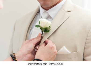 Groom has helping hands with manicure assisting him in pinning his flower rose boutonniere on the lapel of his suit.