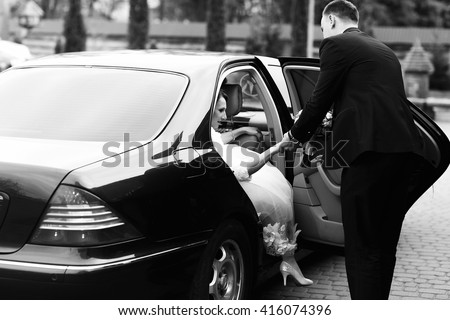 Groom helps bride to go out of the black Mercedes