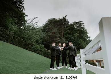 groom and his groomsmen friends in stylish suits drinking whiskey outdoor, morning before the wedding preparation, emotional group of friends celebrating