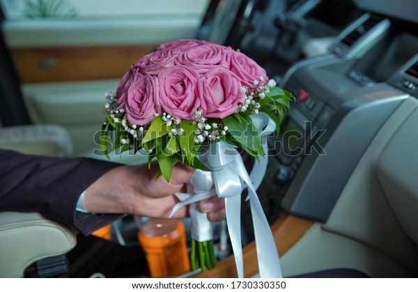 The groom was holding a bouquet of pink flowers in the\
car . woman holding engagement flowers, pink roses in car . Bali\
Catering .