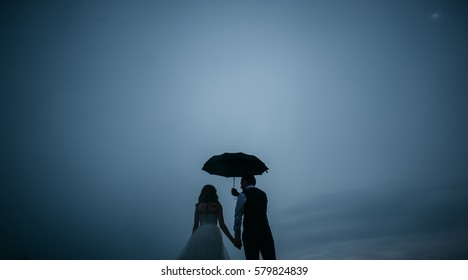 Groom holding an umbrella over the bride on a background cloudy dark blue summer sky - Powered by Shutterstock