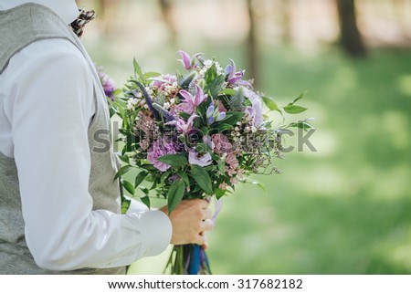 groom holding a wedding bouquet of flowers and greenery