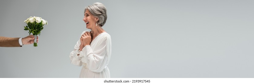 Groom Holding Wedding Bouquet Near Happy Middle Aged Bride In White Dress Isolated On Grey, Banner