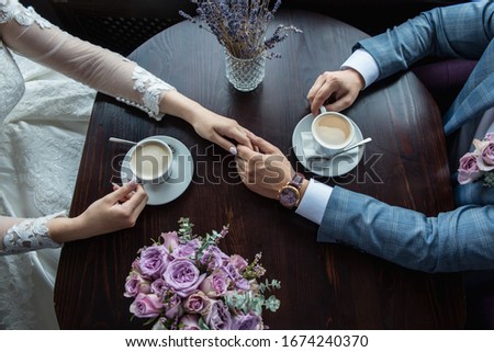 groom holds the hand of the bride in the palm on the background of the bride's bouquet they are sitting at a table and drinking coffee, close-up