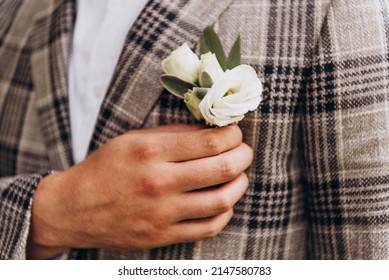 The groom holds a white rose boutonniere in his hand. Men's suit. Wedding, outdoor ceremony.