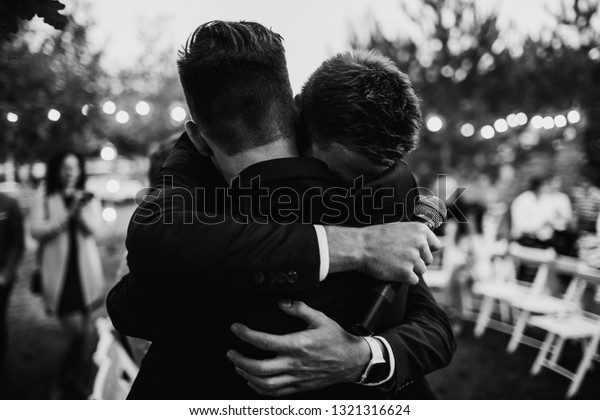 A\
groom is hugging with a best man. Farewell hug\
concept.