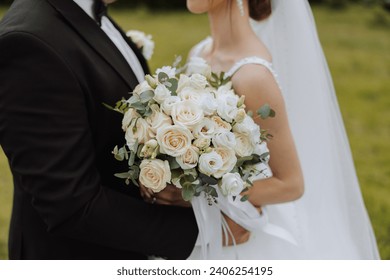 The groom hugs the bride from behind, the bride holds a wedding bouquet. Cropped photo. Groom in a black suit. Details - Powered by Shutterstock