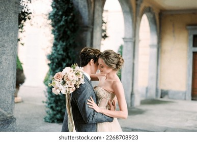 Groom hugs bride with a bouquet of flowers near the arches of an old villa. Como, Italy - Shutterstock ID 2268708923