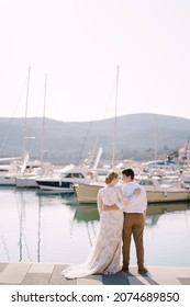 Groom Hugs Bride On The Pier By The Sea In Front Of The Parked Yachts