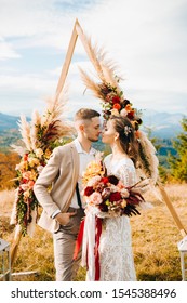 The groom hugs his bride standing under the arch outdoors. Wedding in rustic style