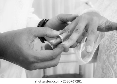 The groom inserting a wedding ring into the bride's finger in black and white