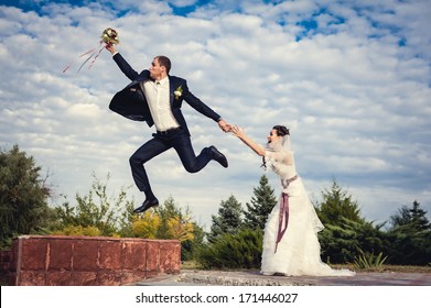 Groom jump up and fly away. Happy young bride and groom outside on their wedding day - Copy space. Wedding couple - new family! wedding dress. wedding bouquet of flowers