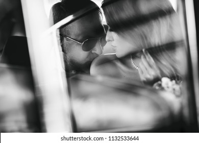 Groom kisses bride's shoulder tender while they sit together inside a retro car