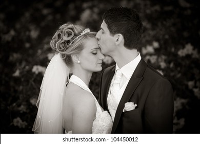groom is kissing his bride very tender on forehead. black and white photo.