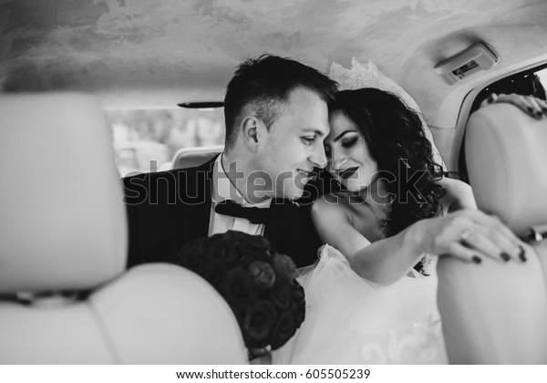 Groom leans to tender bride sitting with her on back\
seat of the car