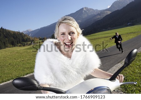 Groom running after bride on motor scooter in rural area