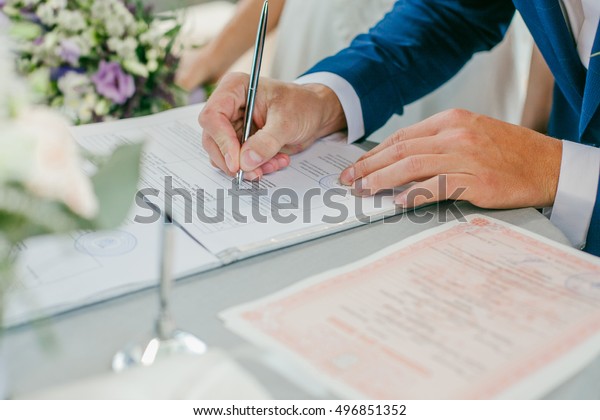 The\
groom signs the marriage registration documents. Young couple\
signing wedding documents. Man signs the\
documents