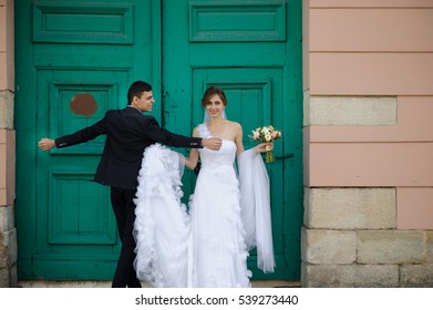 Groom spreads his hands standing with bride before large green door - Powered by Shutterstock