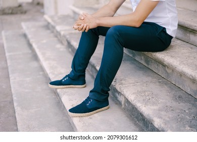 Groom in trousers and sneakers sits on the stone steps