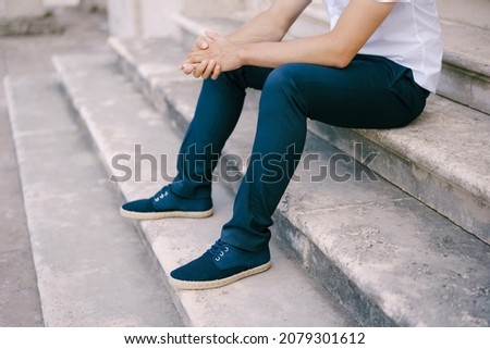 Groom in trousers and sneakers sits on the stone steps