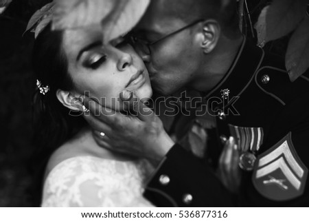 Groom in uniform of US Army holds bride's face tender while kissing her