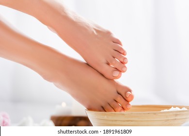 Groomed Female Feet With Glossy Pink Toenails Near Wooden Bowl On White