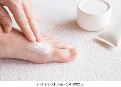 Groomed Man's Hands Applying Feet Moisturizing Cream. Bare Feet On The White Towel. Cares About Clean And Soft Legs Skin. Healthcare Concept.