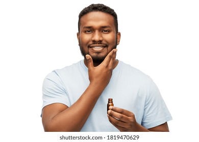 grooming and people concept - smiling young african american man applying lotion or beard oil over white background