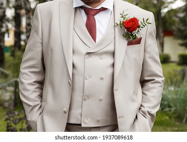The groom's light beige suit with a boutonniere and a red tie close-up.