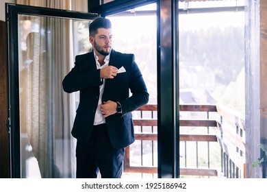 Groom's morning before the wedding. Morning preparation. A young and handsome man is dressing in a wedding suit by the window. - Shutterstock ID 1925186942