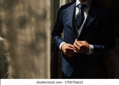 Grooms morning preparation. Cropped photo of elegant young fashion man dressing up for wedding celebration. Groom dressed in modern blue formal suit, white shirt getting ready for event. Sunny morning - Powered by Shutterstock