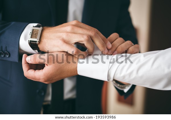 Groomsman helps to\
groom to put on\
cufflinks