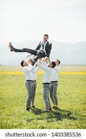 Groomsmen and groom playing outdoors on the wedding day. Funny wedding moment for best groom friends. Man hug each other. - 
