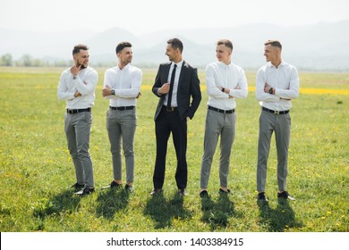 Groomsmen and groom posing outdoors on the wedding day. Funny wedding moment for best groom friends. Man hug each other. - 