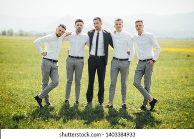 Groomsmen and groom posing outdoors on the wedding day. Funny wedding moment for best groom friends. Man hug each other. - 